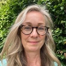 Naomi Proudlove, a white woman with blond hair and tortoiseshell glasses, looking at the camera and smiling