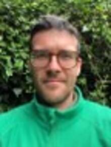 Seb Tighe, a white man with dark brown hair and glasses, wearing a green fleece, looking at the camera