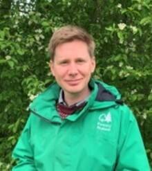 William Tyson, a white man with short light brown hair, wearing a green jacket, standing outside and looking at the camera