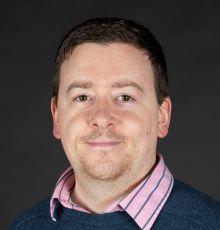 David Johnson, a white man with short brown hair wearing a blue jumper and pink shirt, looking at the camera