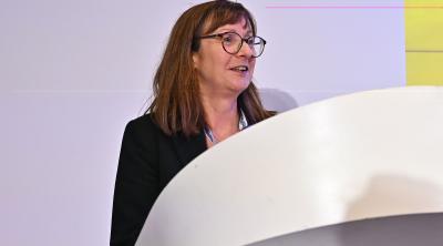 Ann Carruthers, a white woman with glasses standing behind a white lectern