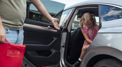 child exiting vehicle in school uniform. man holding school book bag