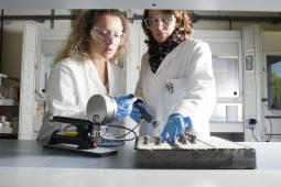 image showing two science and engineering professionals in white coast and safety goggles, testing an experimental piece of road surface