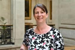 Angela Jones, a white woman in her late 40s, with shoulder-length brown hair, brown eyes, wearing a floral top and looking at the camera, leaning on a balustrade