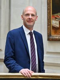 Andrew Cook, a white man, bald, in his late forties, wearing a blue suit and pale shirt with a dark tie, looking at the camera