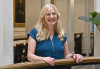 Carolyn McKenzie, a white woman with long blond hair, wearing a teal top, looking at the camera and smiling.