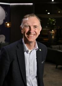 Nigel Riglar, a white man in his late fifties, with short grey hair, wearing a dark jacket and pale shirt, looking at the camera and smiling